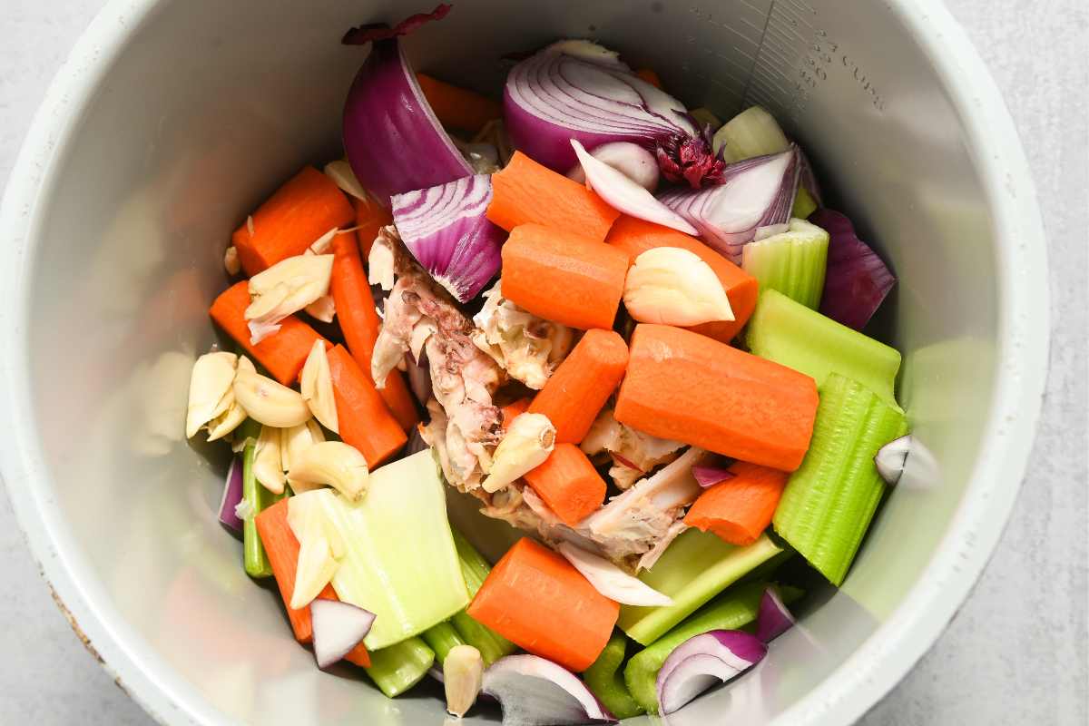 raw vegetables and chicken bones in a pot.