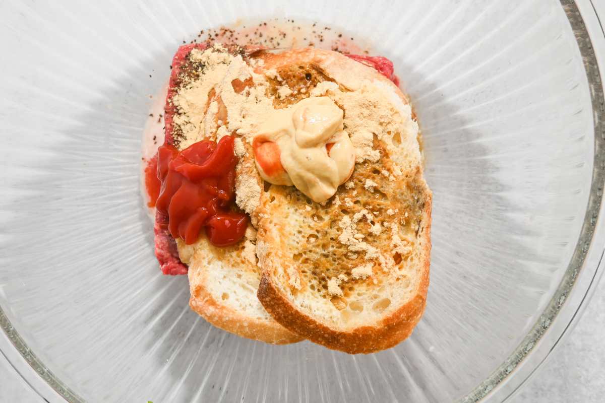 bread on top of meat with seasonings, ketchup, and mustard.
