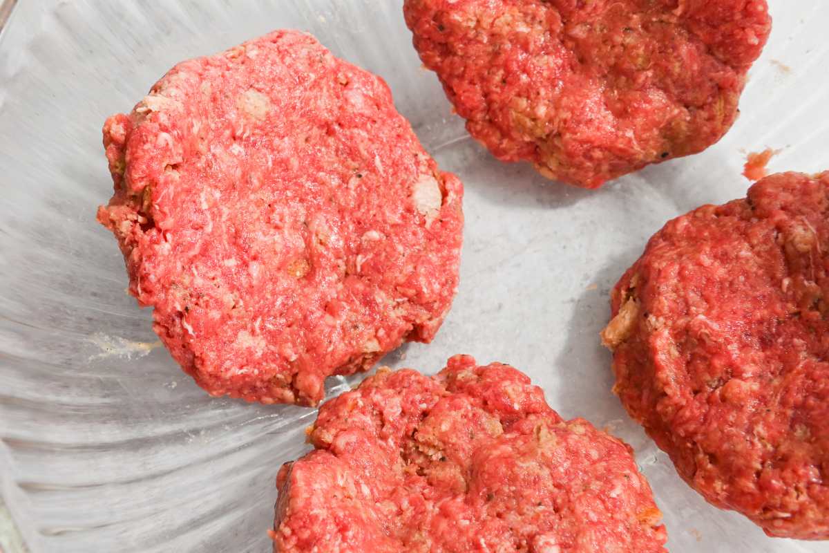 uncooked burger patties in a glass bowl.