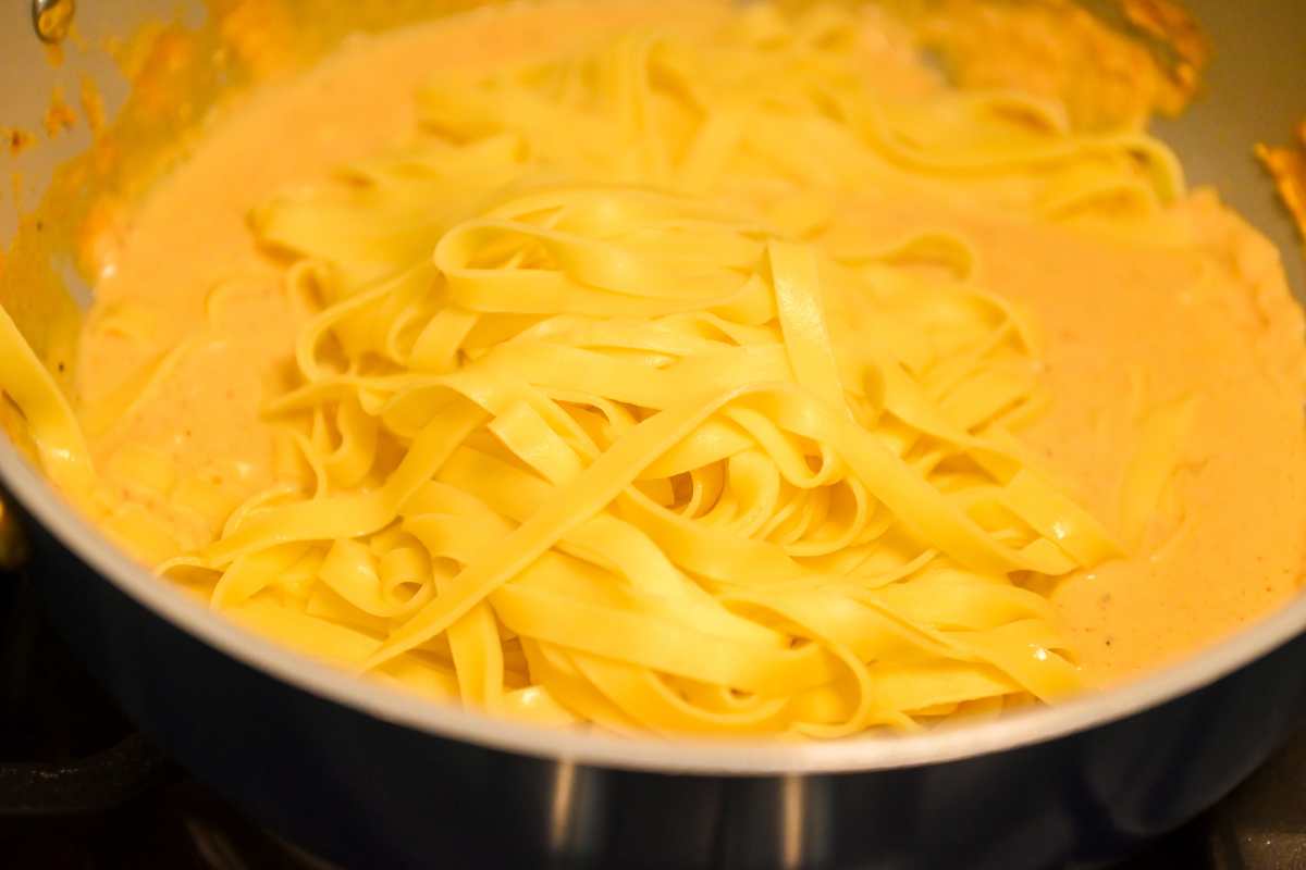 cooked pasta going into creamy sauce.
