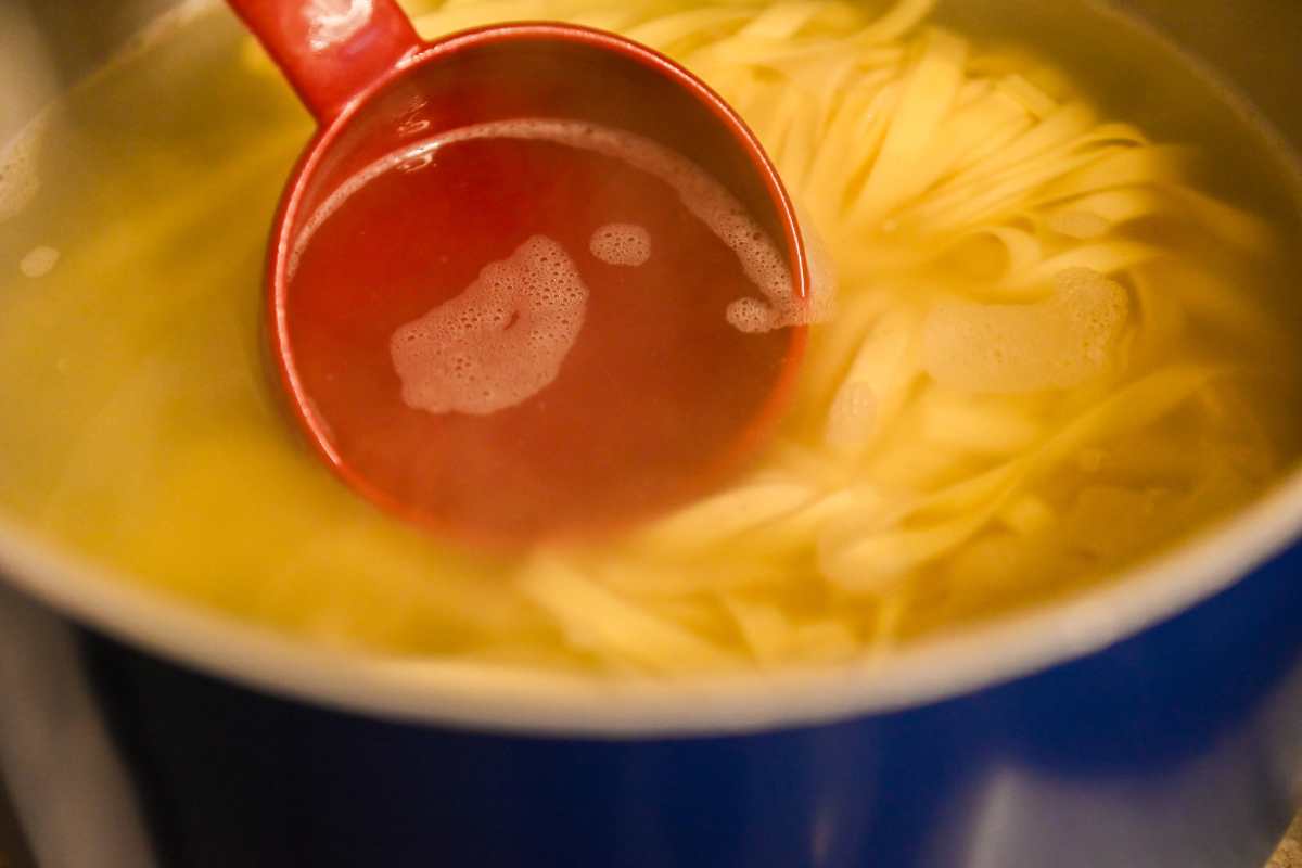 red measuring cup taking pasta water out of a pot with pasta.