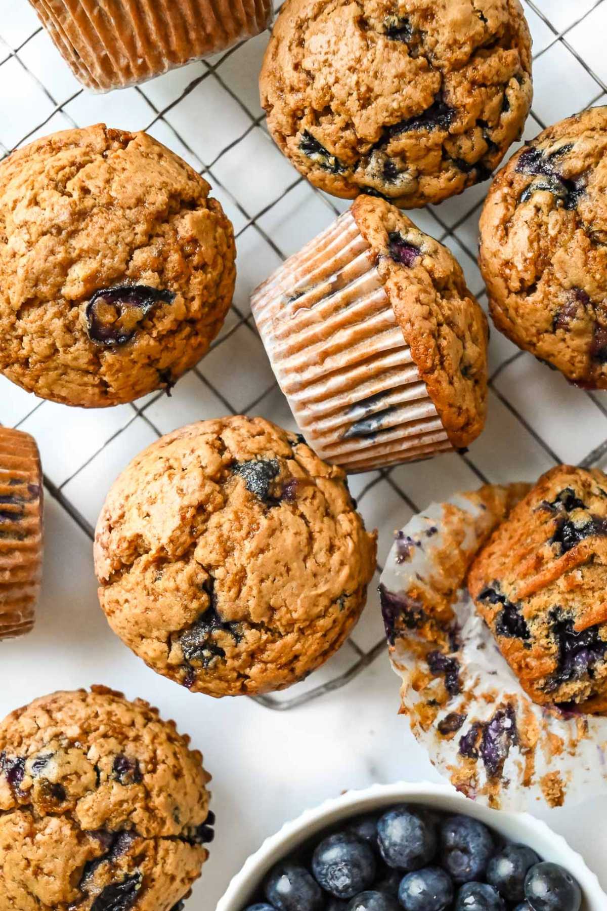 many protein blueberry muffins on a cooling rack next to a white bowl of blueberries.
