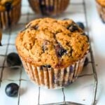 one blueberry protein muffin in the foreground on a cooling rack.