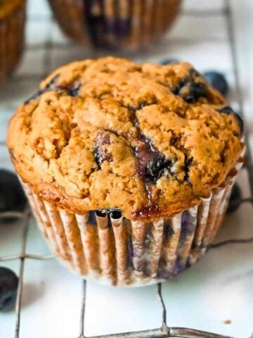 one blueberry protein muffin in the foreground on a cooling rack.