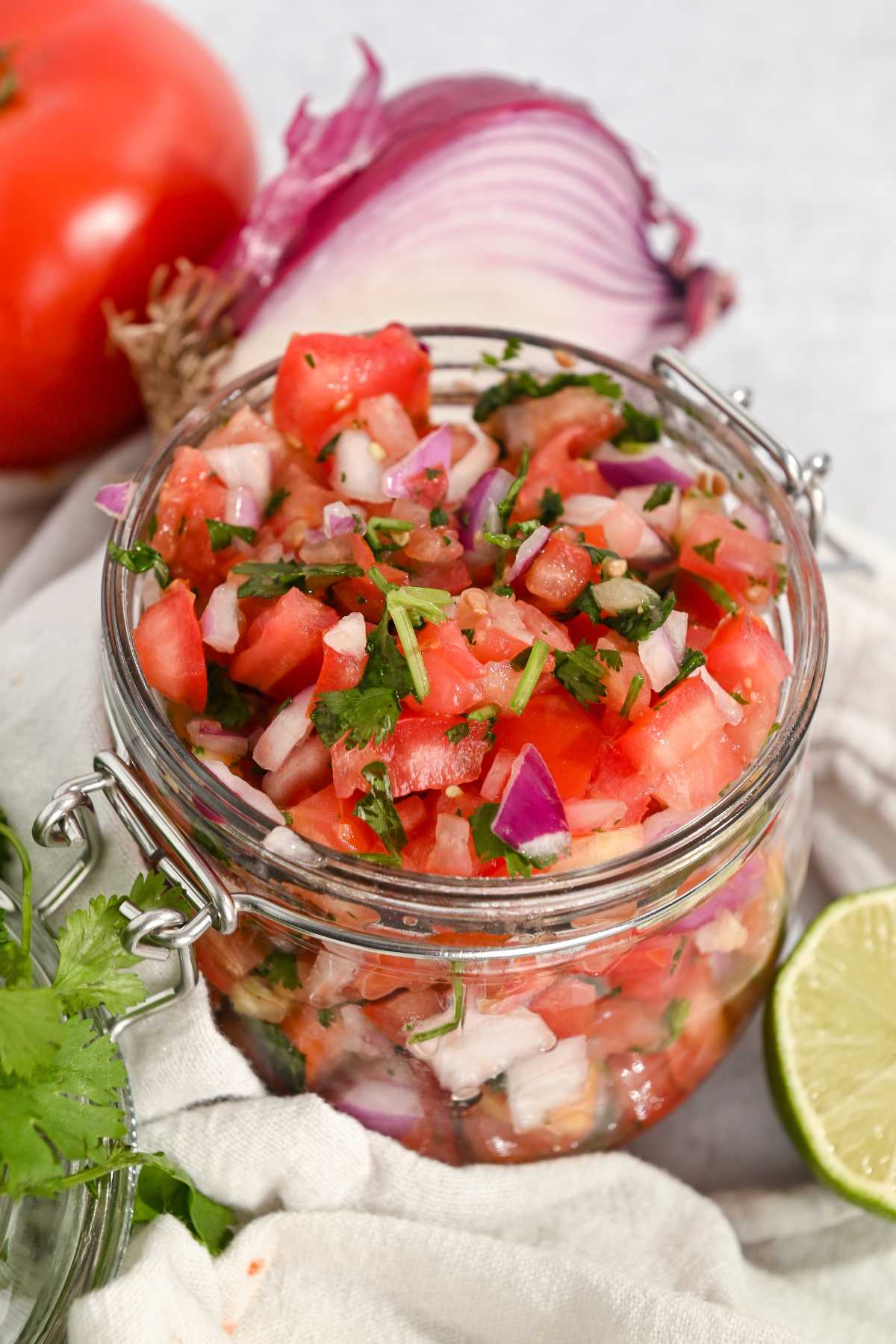 mild pico de gallo salsa in a glass jar with ingredients around it.