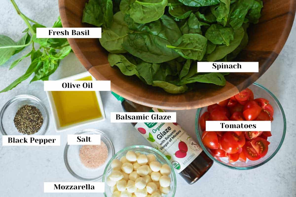 labeled ingredients for making spinach caprese salad on a gray background.