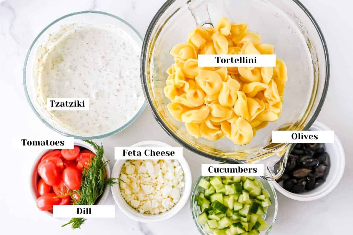 labeled ingredients for Greek tortellini salad on a white background.
