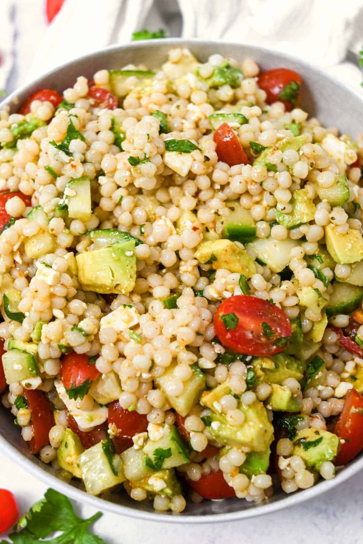avocado couscous salad in a white bowl on a white background.