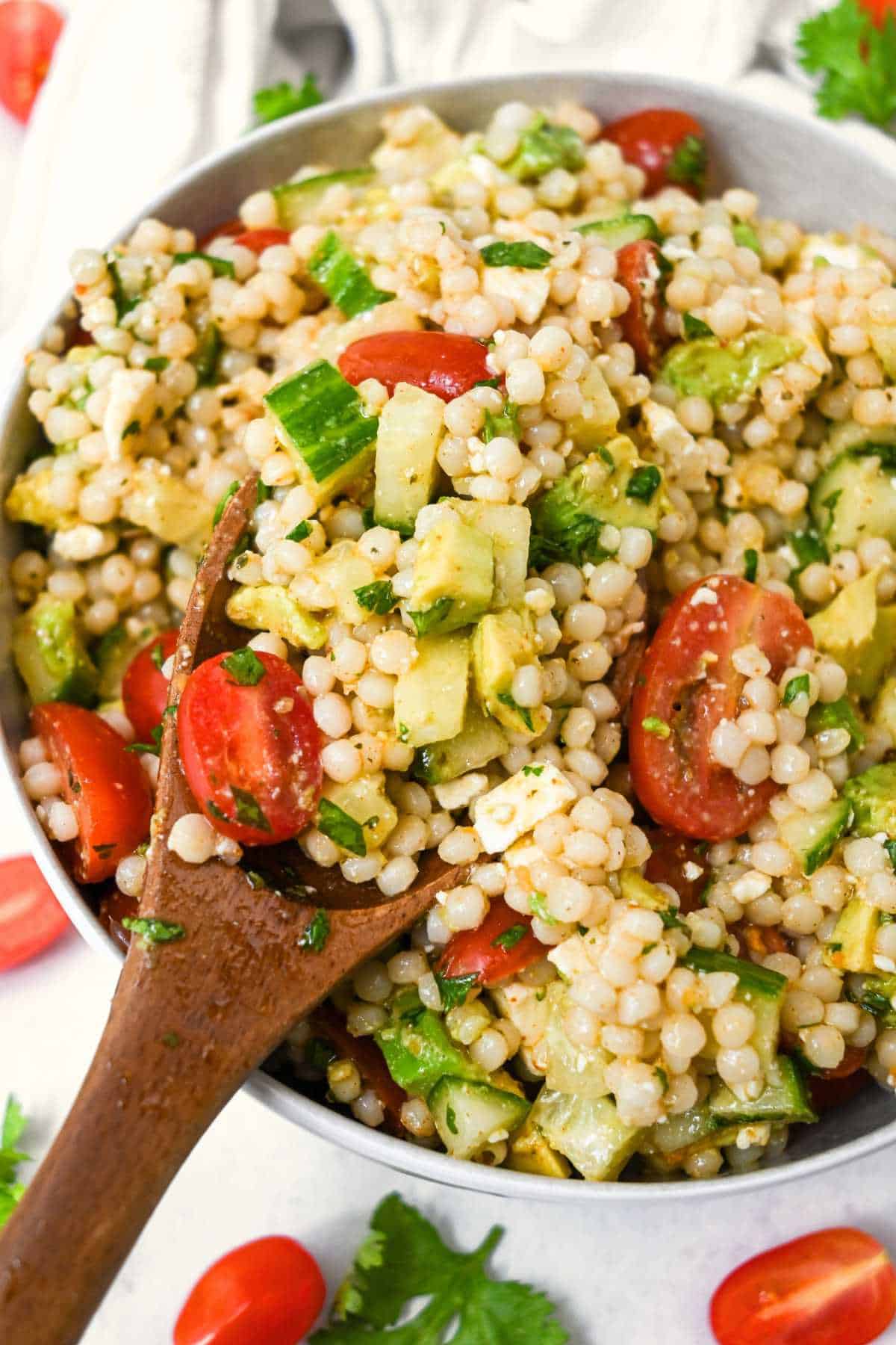 bowl of avocado couscous salad with a wooden spoon.