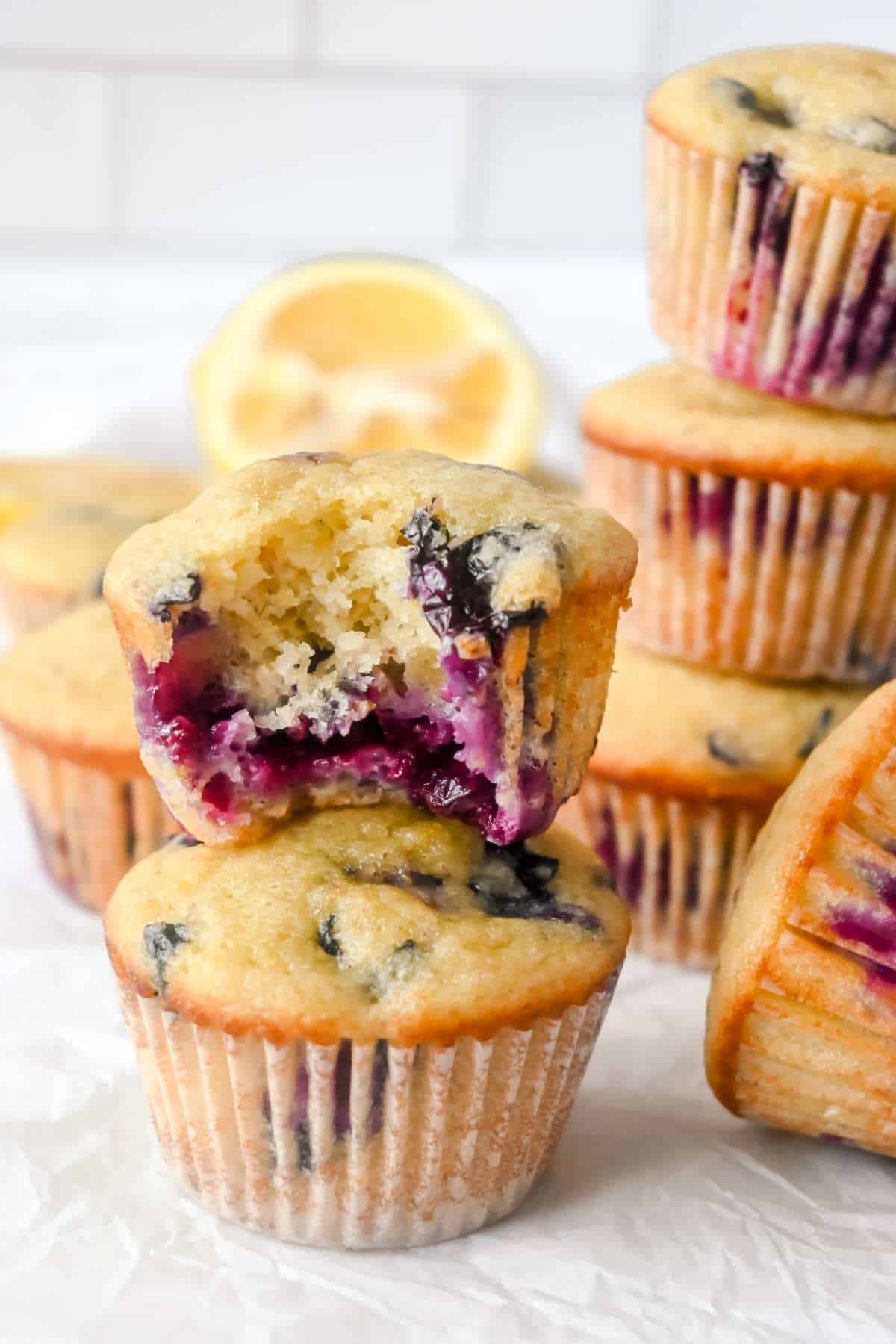 stack of 2 blueberry lemon protein muffins on a white background with a bite shot on the top muffin.
