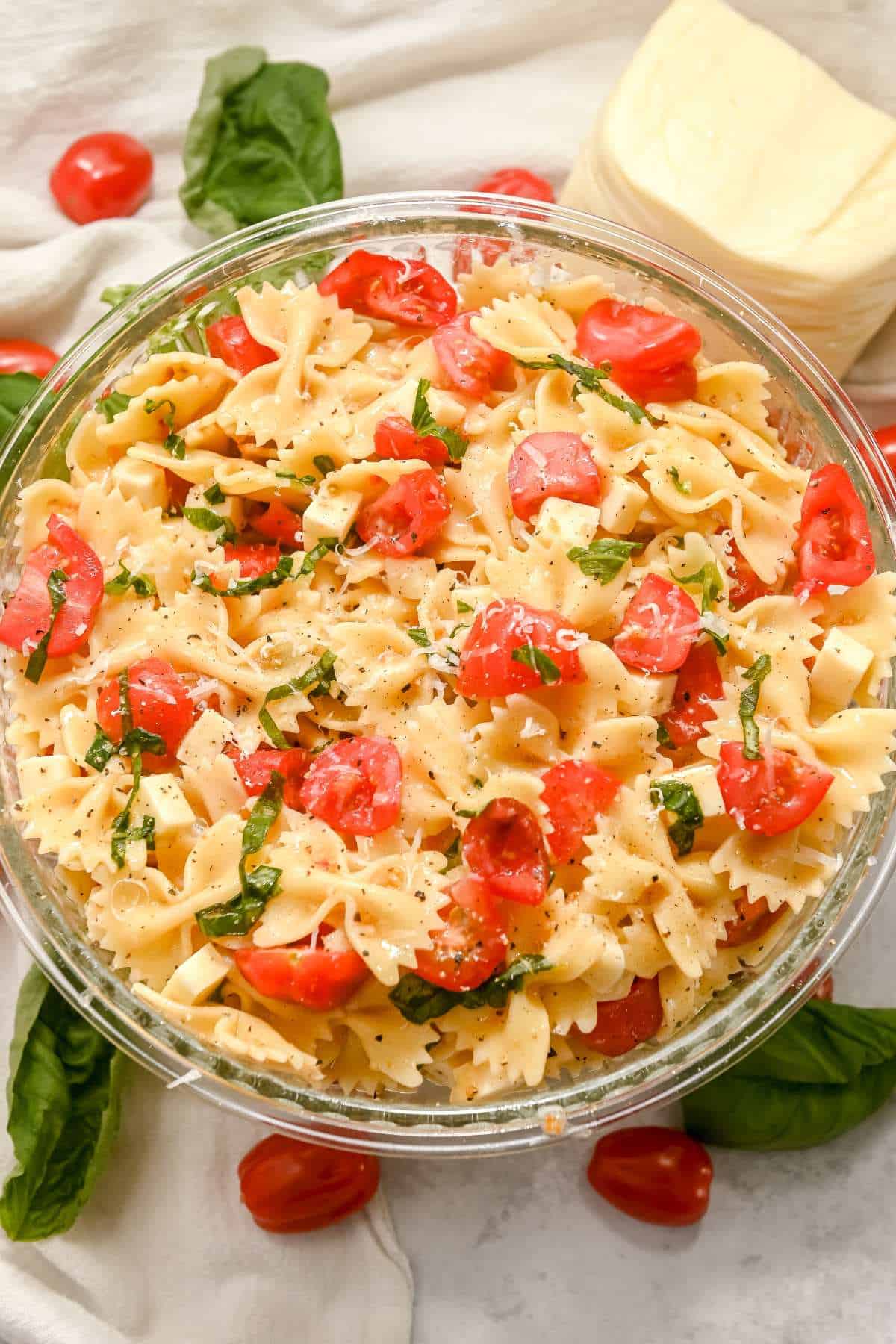 bowl of caprese pasta salad with bow tie pasta on a gray background with ingredients around it.