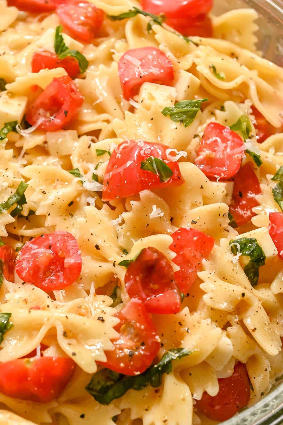 very close shot of bow tie caprese pasta salad with cherry tomatoes and basil.