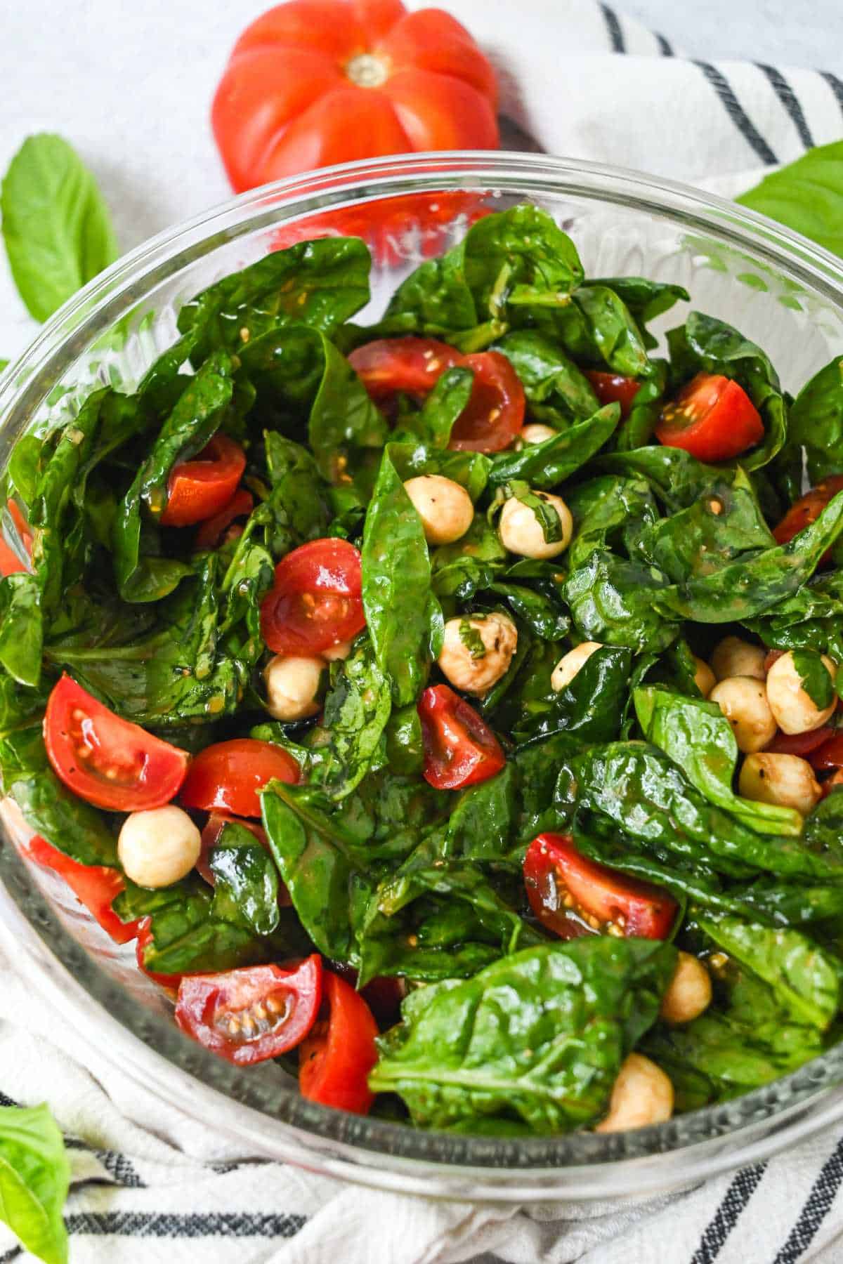 bowl of fresh caprese salad with spinach and tomatoes on a white towel with blue stripes.