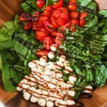 close up of sectioned ingredients for caprese spinach salad drizzled with balsamic glaze.