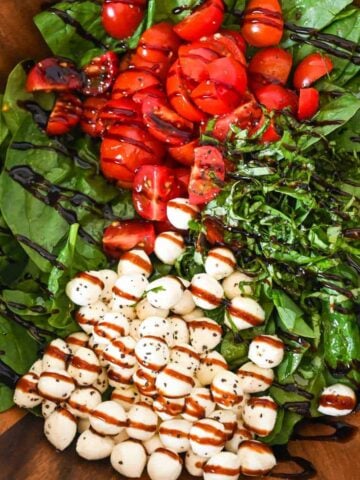 close up of sectioned ingredients for caprese spinach salad drizzled with balsamic glaze.