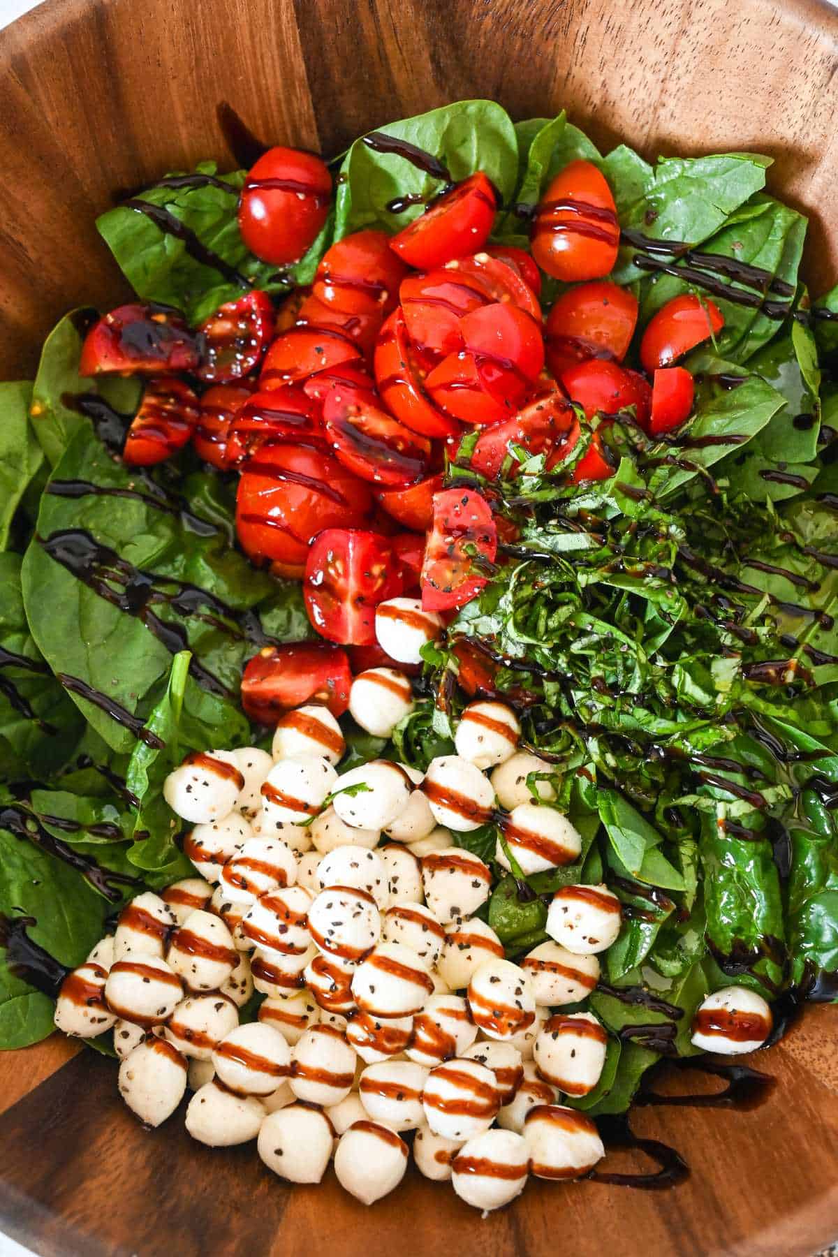 ingredients for caprese spinach salad in a bowl drizzled with balsamic glaze.