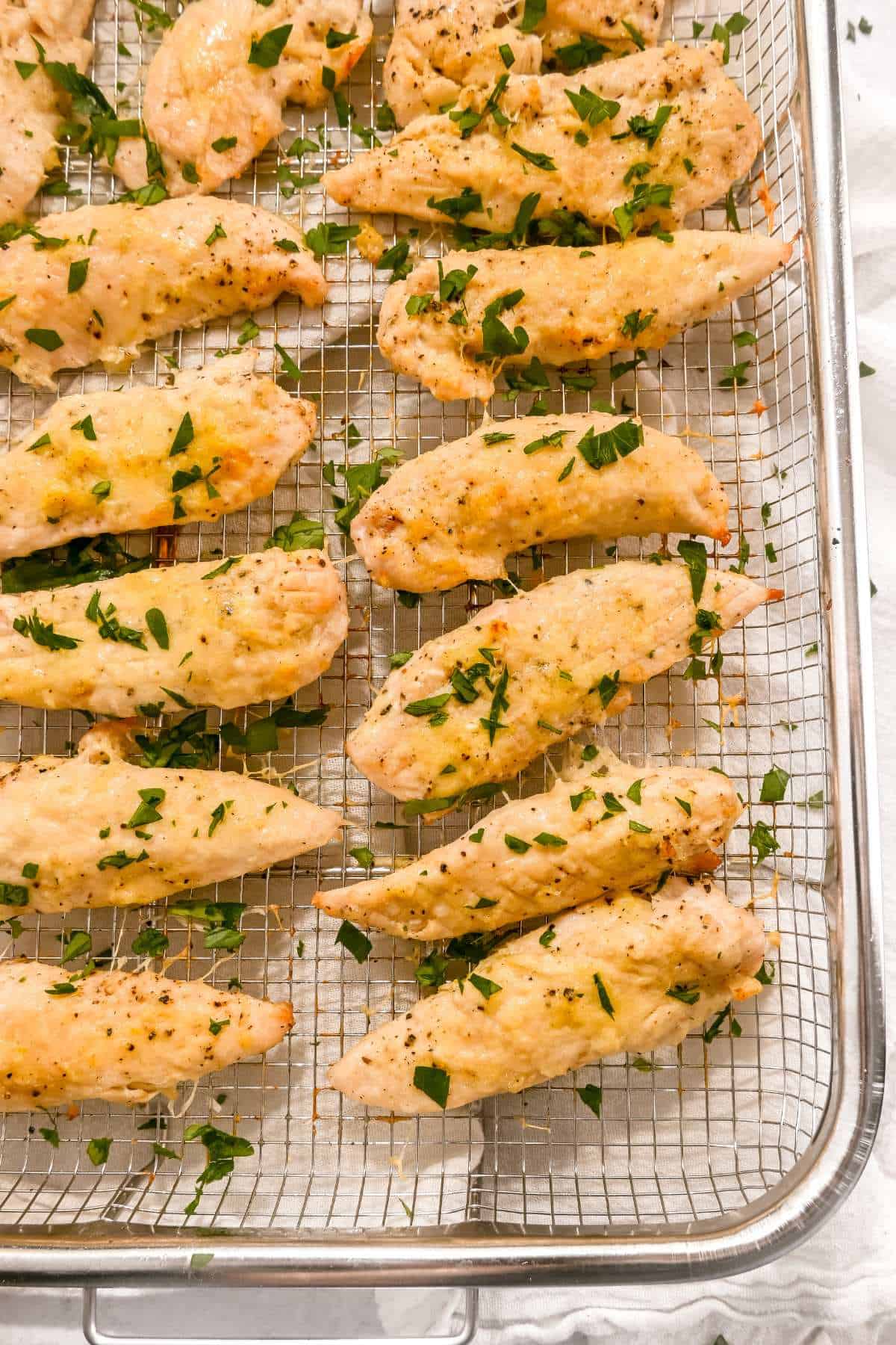 garlic parmesan chicken tenders topped with parsley on an air fryer pan.