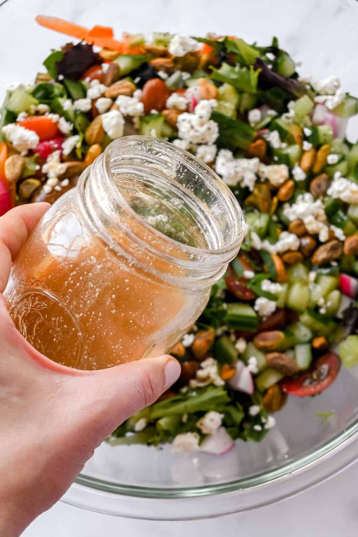 hand pouring red wine vinaigrette over a salad.