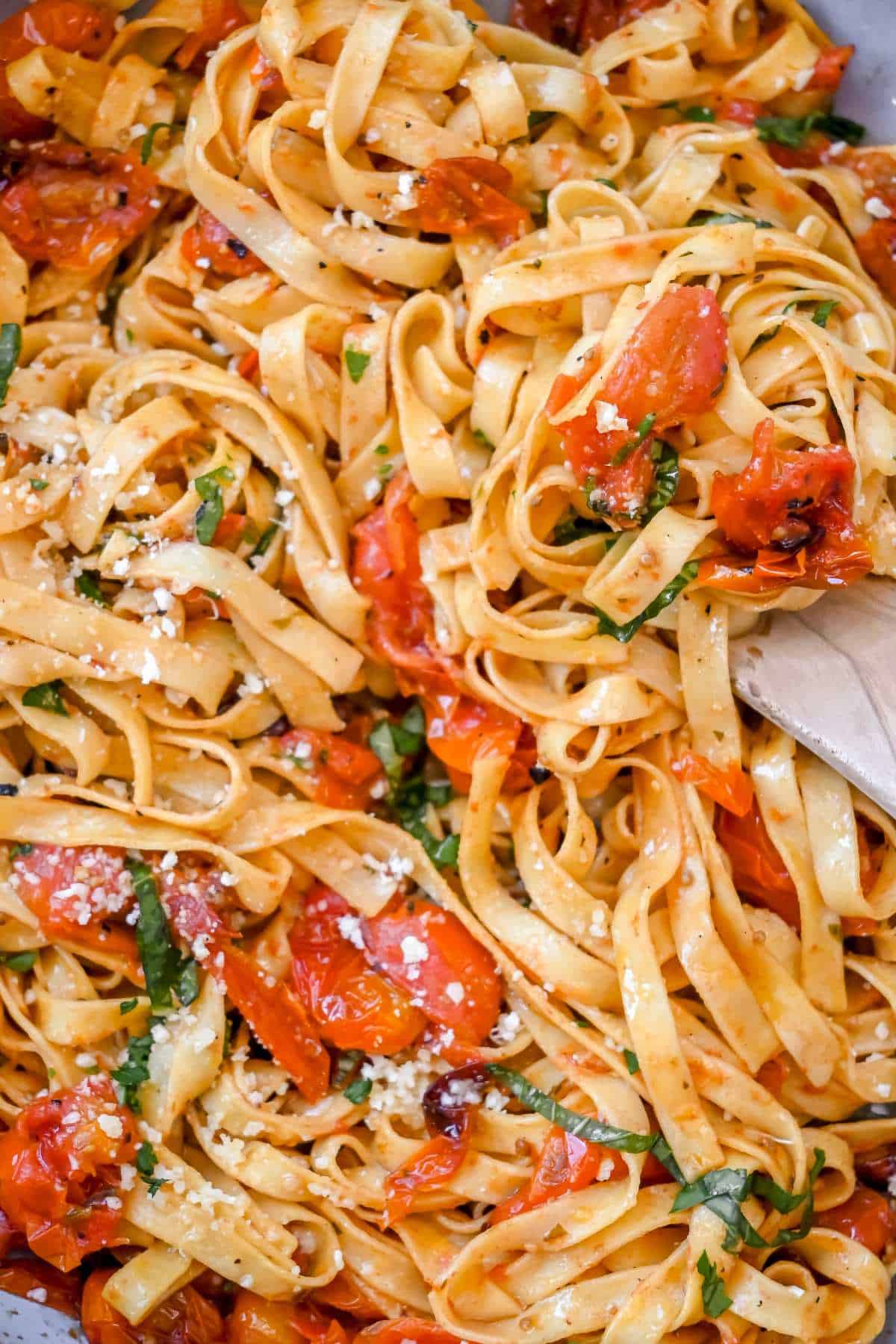 close up of cherry tomato pasta with a wooden spoon.
