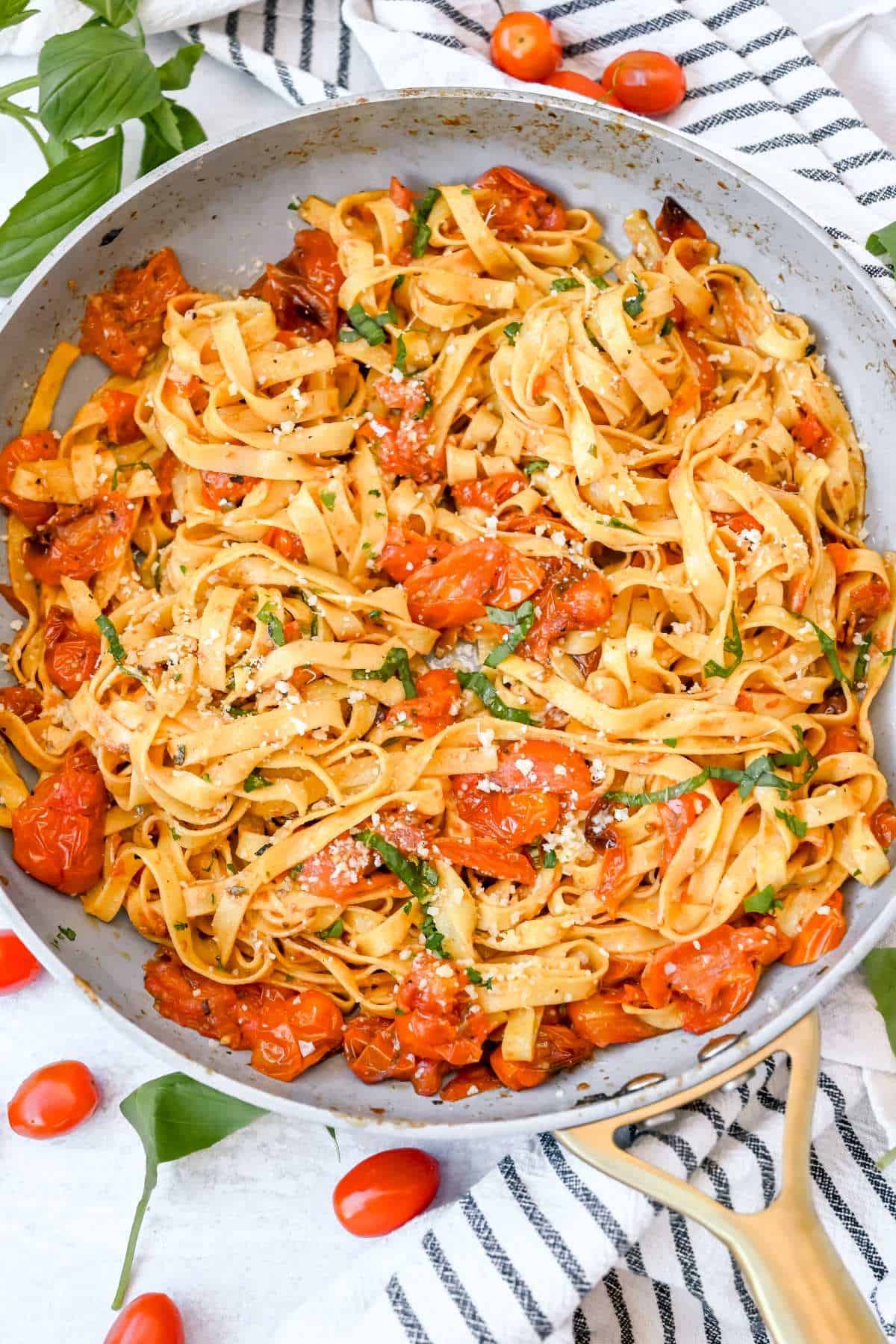 skillet with cherry tomato pasta on a white background with a blue striped towel.