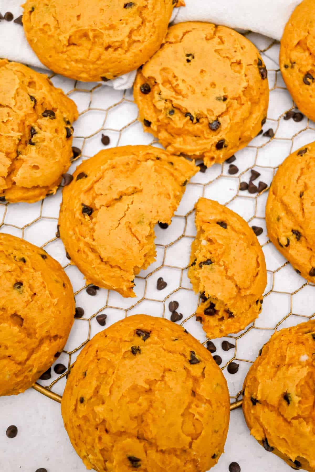 cake mix pumpkin cookies on a cooling rack with one in the center broken in half.