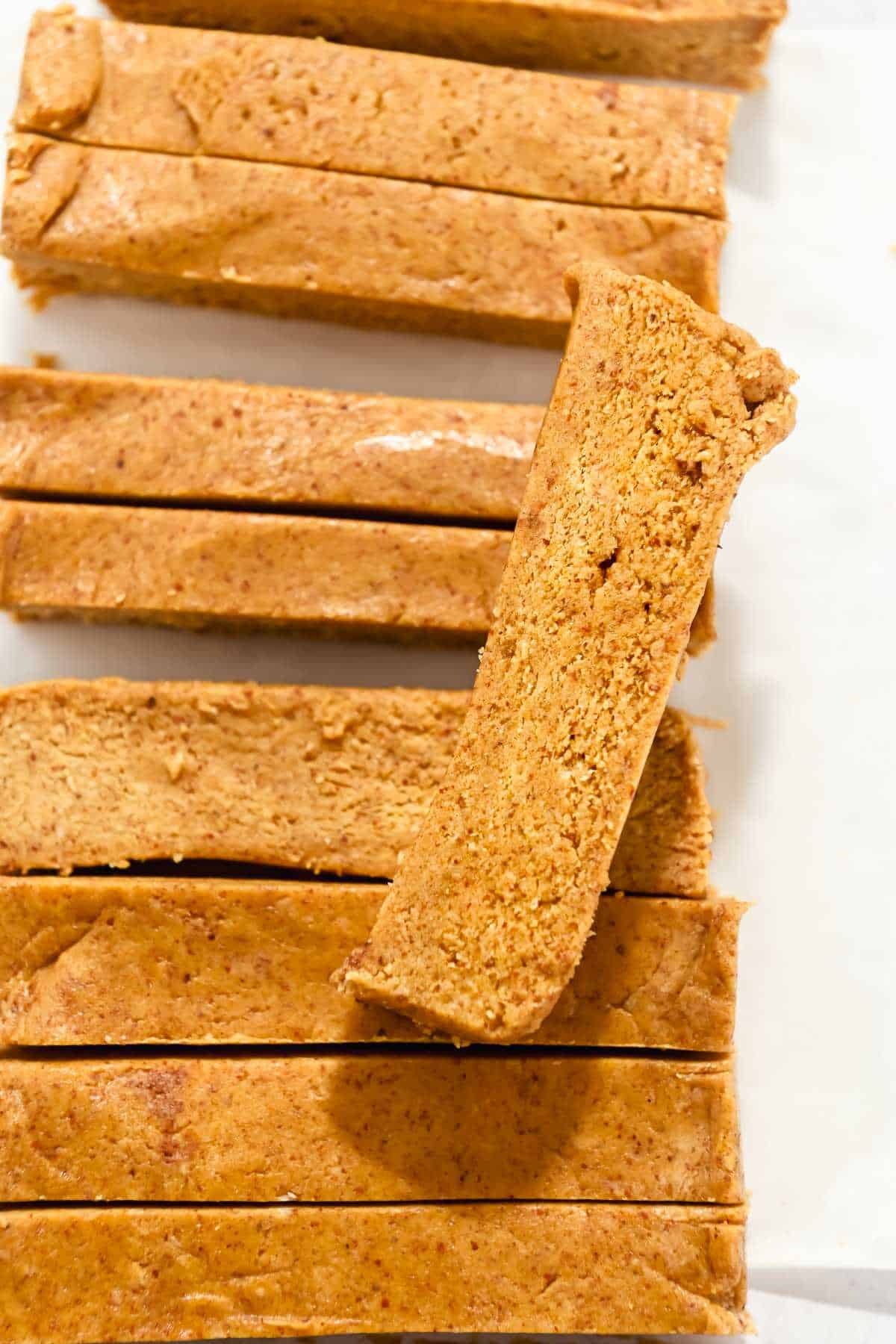 close up of a cut pumpkin protein bar on top of sliced pumpkin protein bars in a line.