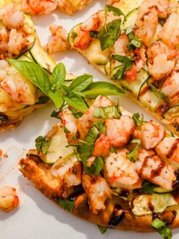 close up shot of a slice of shrimp pizza topped with fresh basil and balsamic glaze.