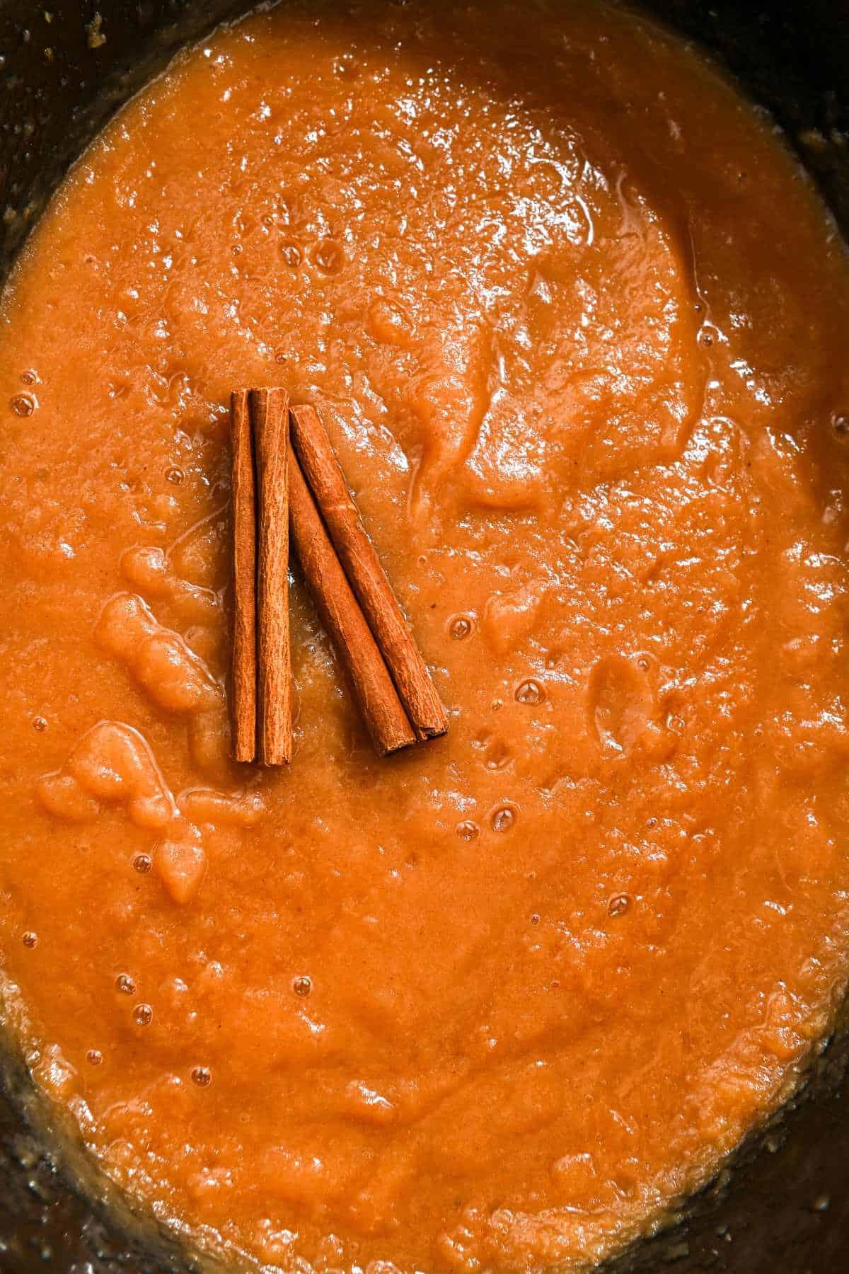 top down view of homemade applesauce in the crockpot with cinnamon sticks on top.