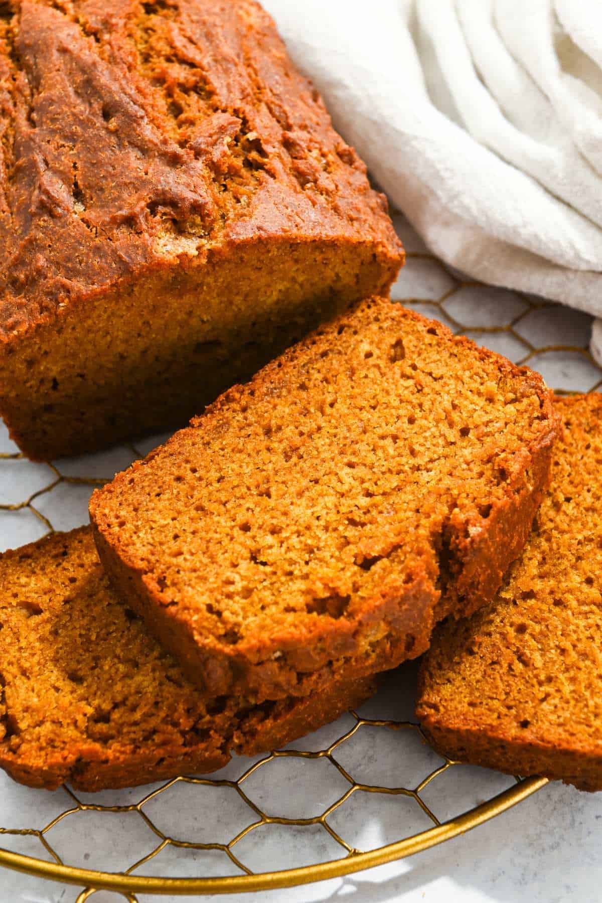 slice of eggless pumpkin bread next to a loaf and with two slices beneath it.