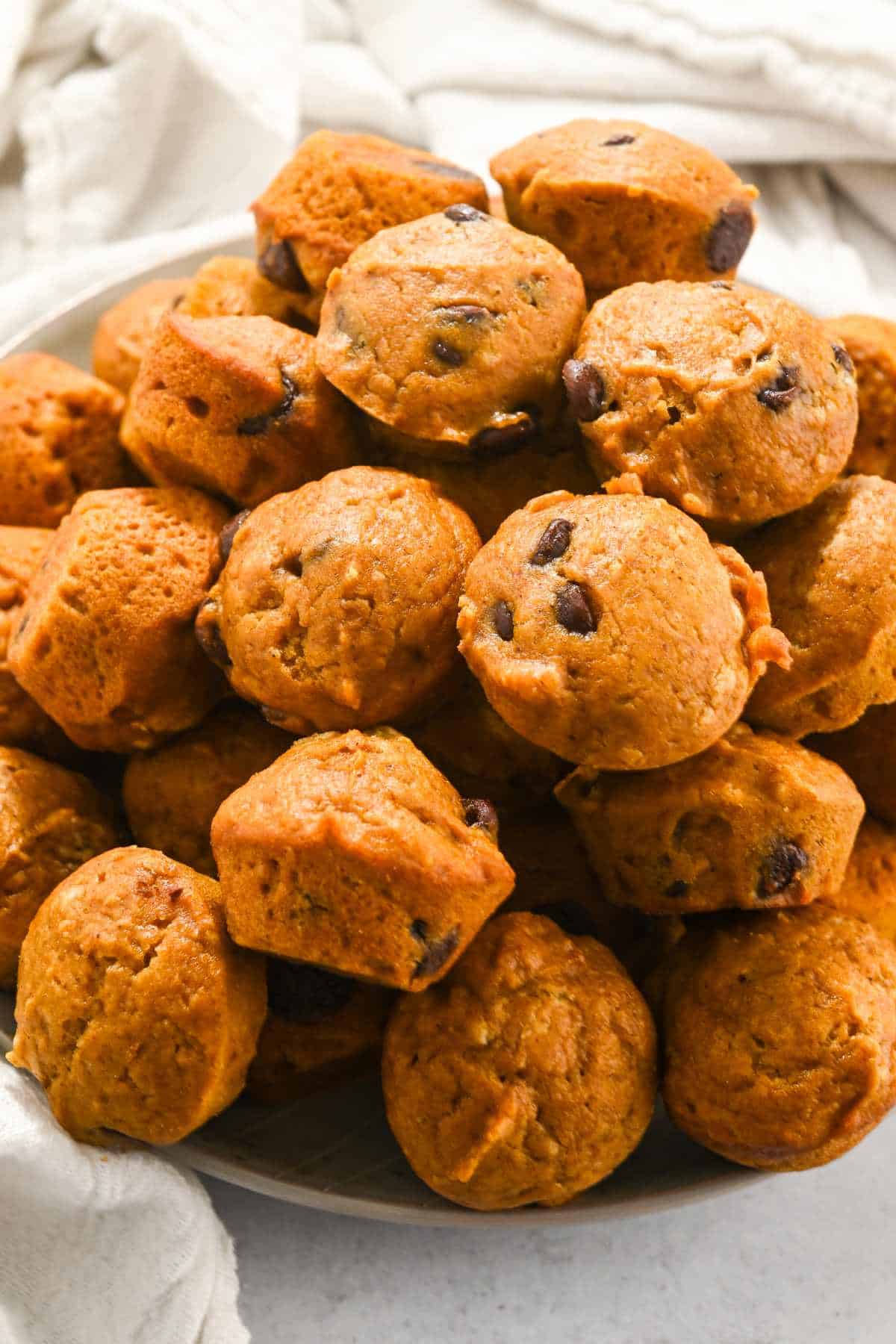 full plate of pumpkin mini muffins in a pile on a white background.