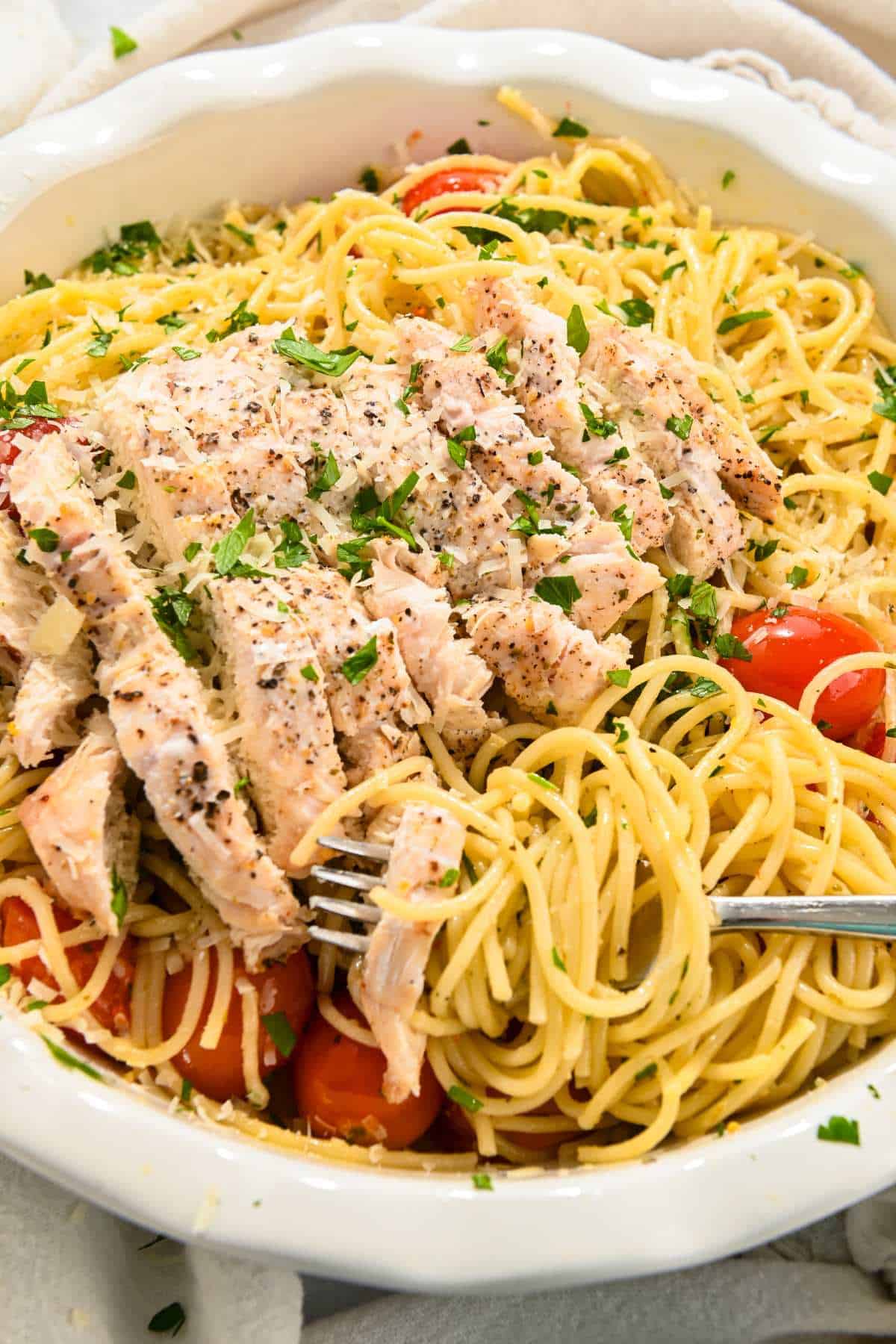 sliced chicken on top of aglio e olio spaghetti in a white bowl.