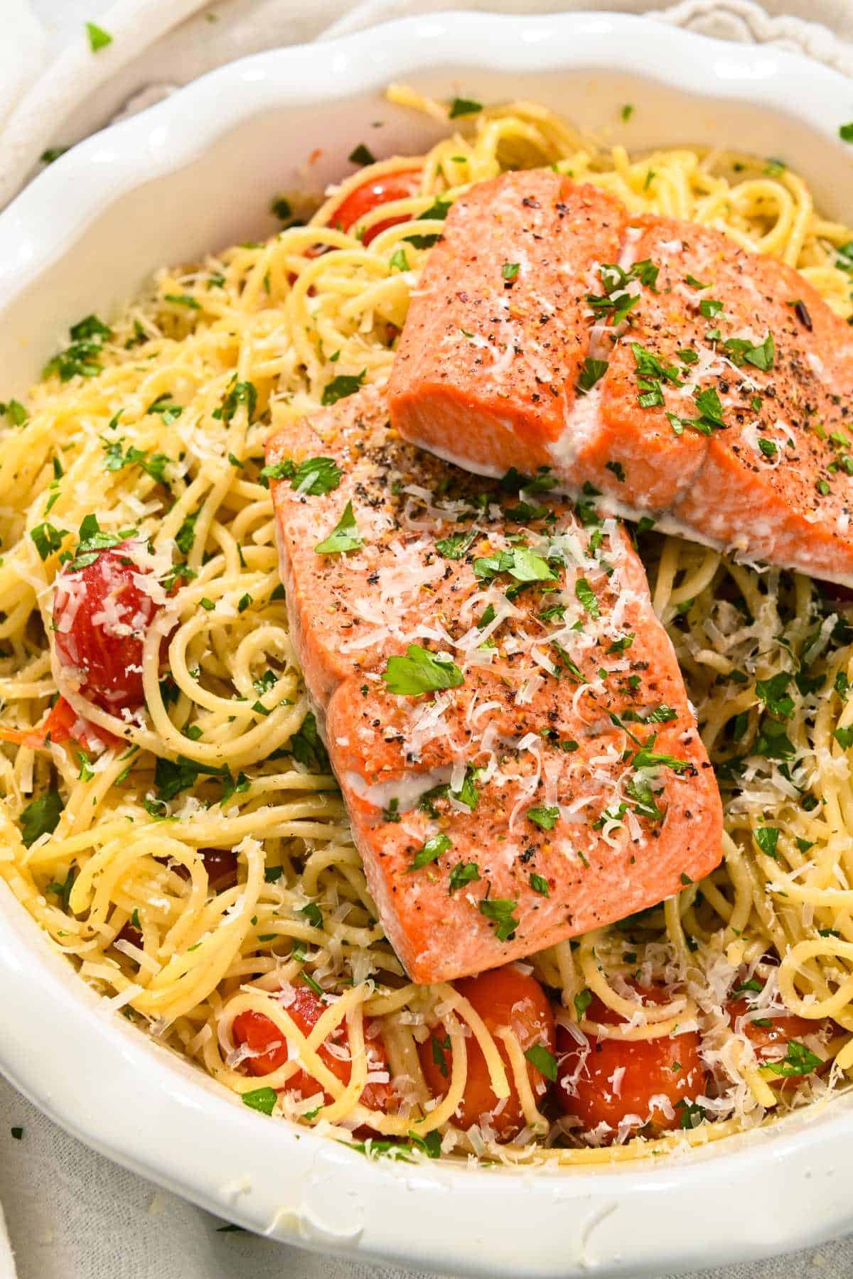 two pieces of salmon on top of spaghetti aglio e olio pasta.