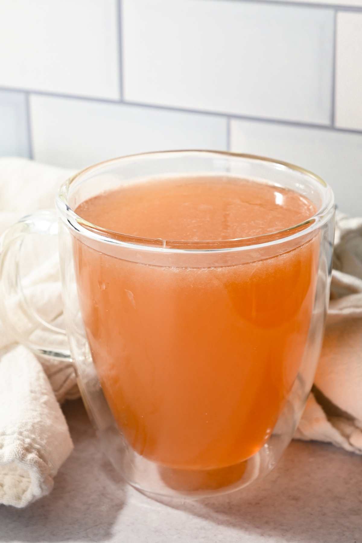 Starbucks honey citrus mint tea in a glass mug in front of a white tile background.