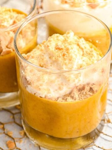 close up of 3 cups of pumpkin pie in a cup topped with whipped cream and graham cracker crumbs.
