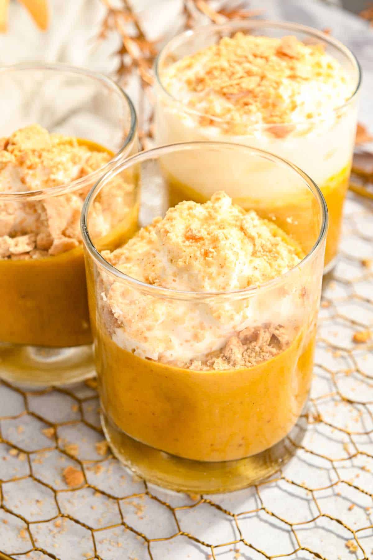 3 cups of pumpkin pie in a cup topped with whipped cream and graham cracker crumbs.