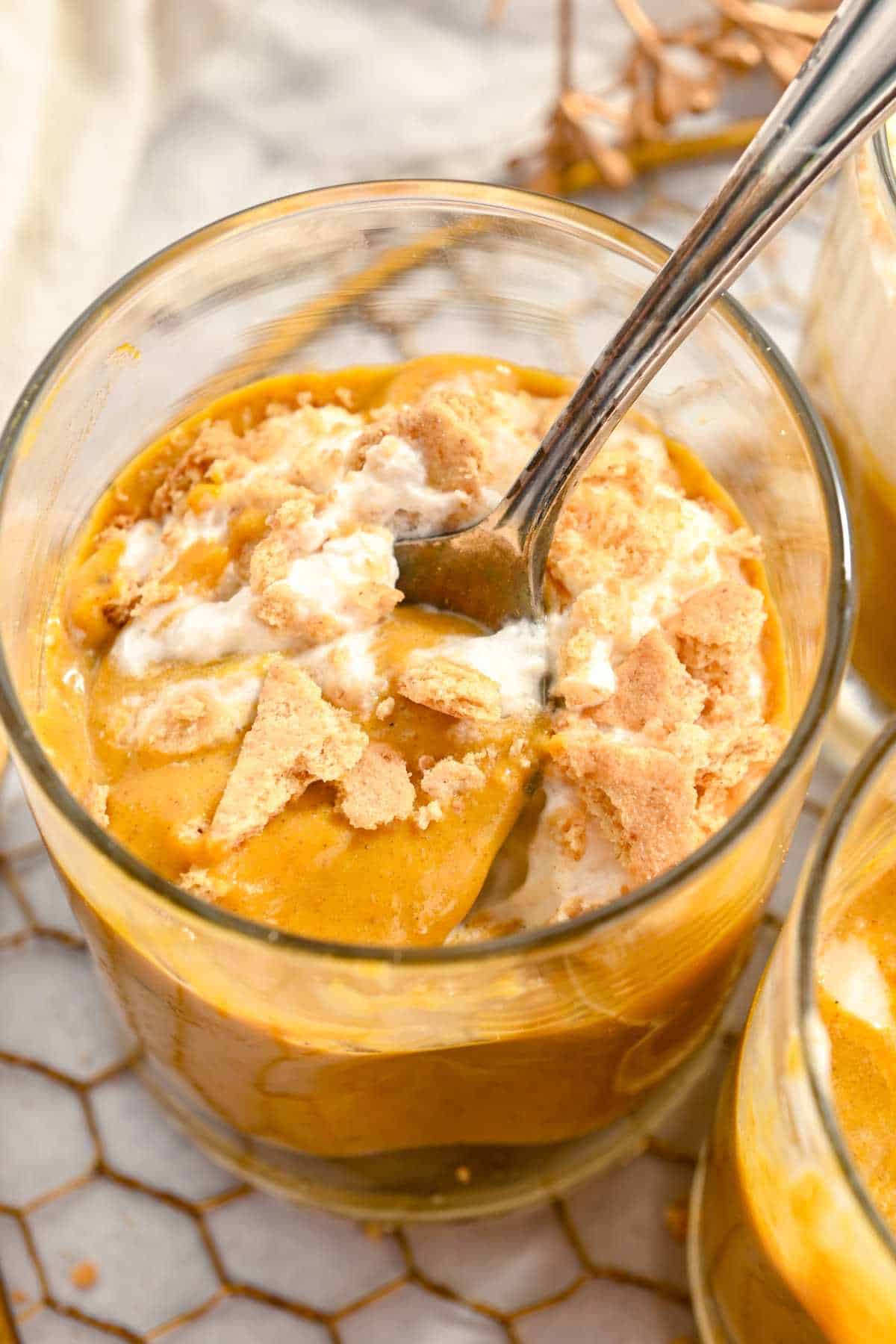top view of pumpkin pie in a cup with a spoon and topped with whipped cream.