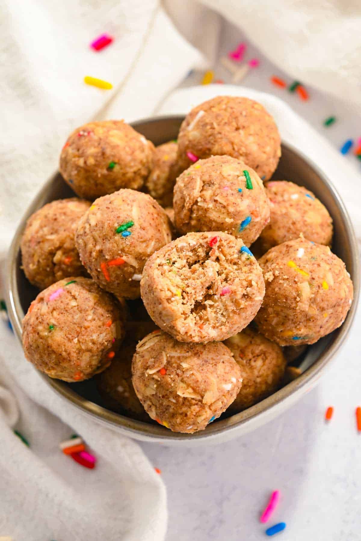 birthday cake protein balls in a white bowl with sprinkles around it.