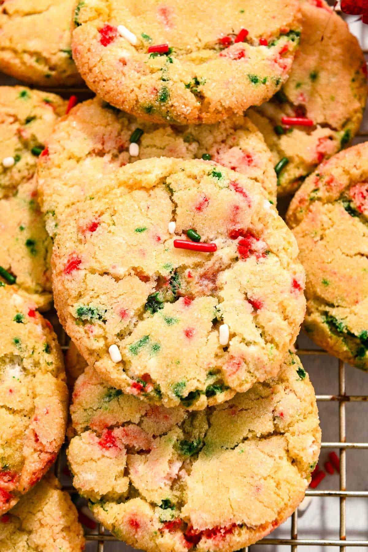 close up shot of one sugar cookie with christmas sprinkles on top of a pile or more cookies.