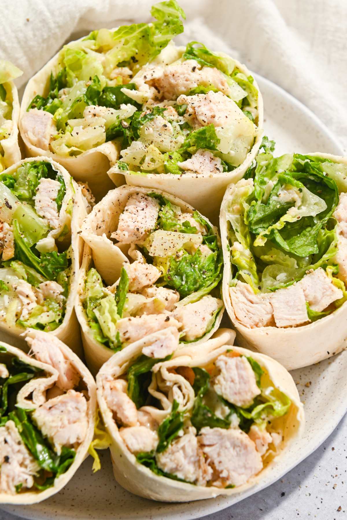 six grilled chicken caesar wraps on a white plate.