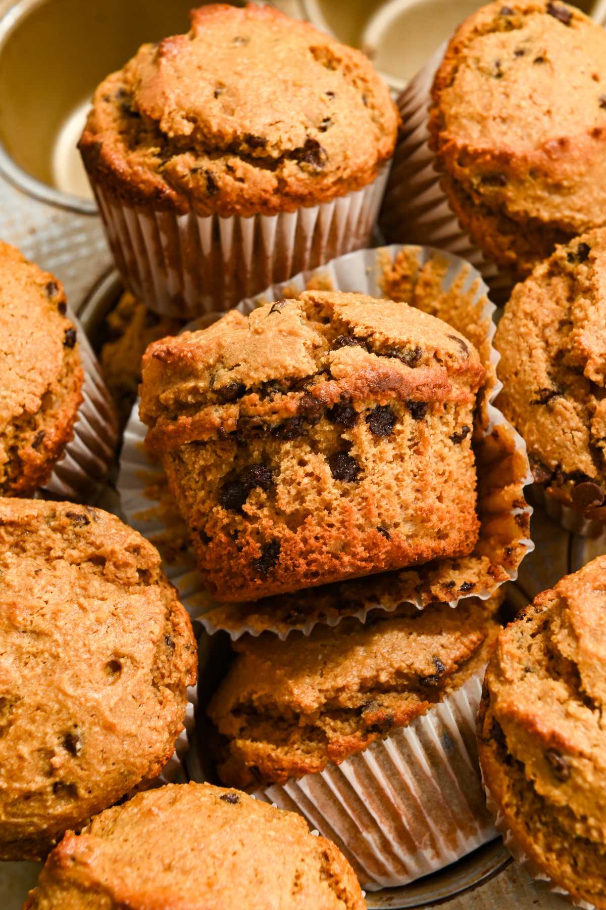 pile of chocolate chip protein muffins with the side view of the middle one.