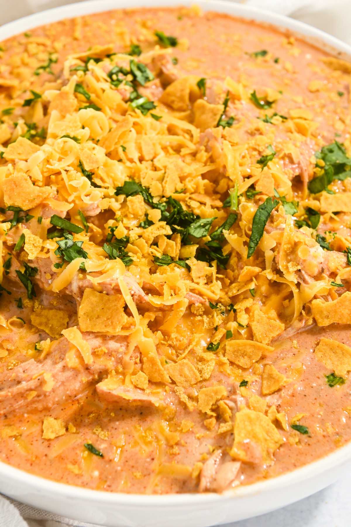 creamy chicken taco soup in a white bowl topped with cheese, tortilla chips, and cilantro.