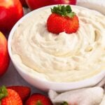 close up of healthy cheesecake dip in a white bowl with a strawberry on top.