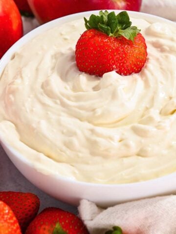 close up of healthy cheesecake dip in a white bowl with a strawberry on top.
