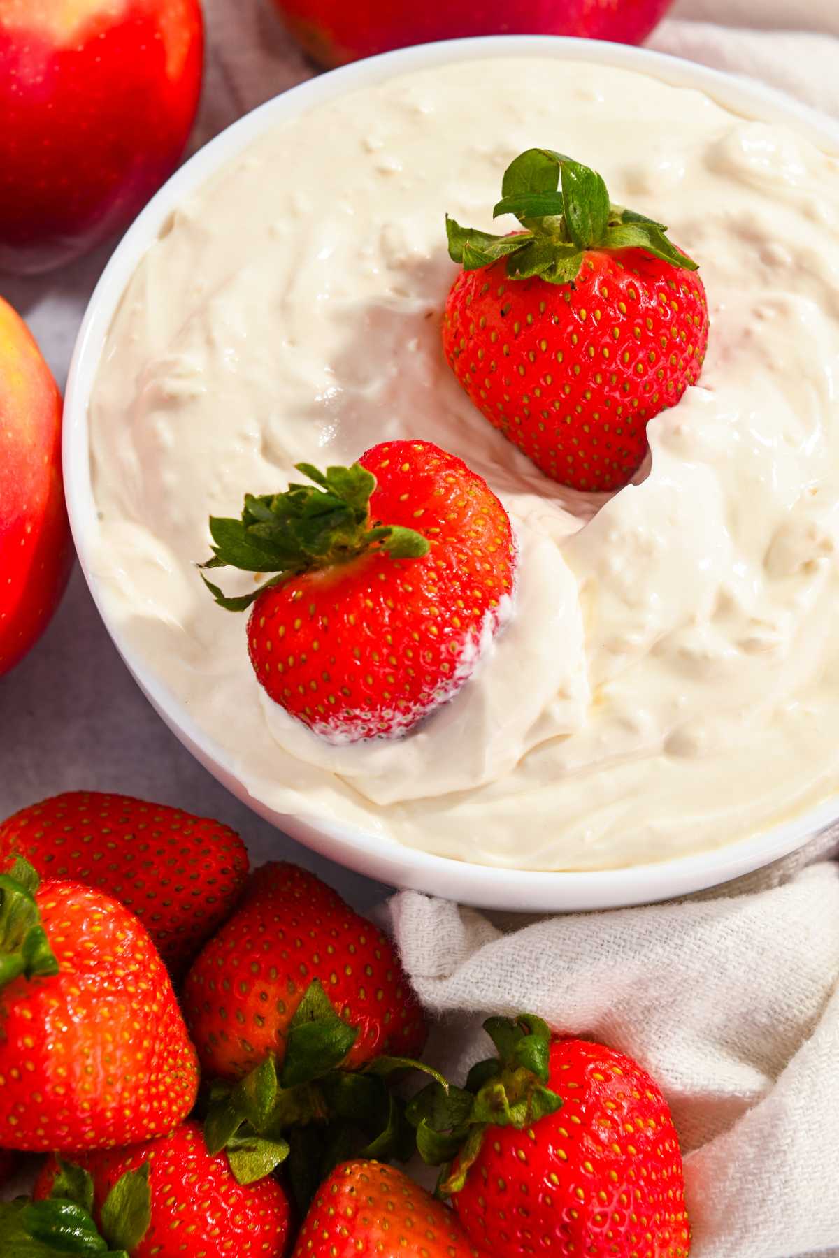 A bowl of healthy cheesecake dip with two strawberries on top and surrounded by fruit.