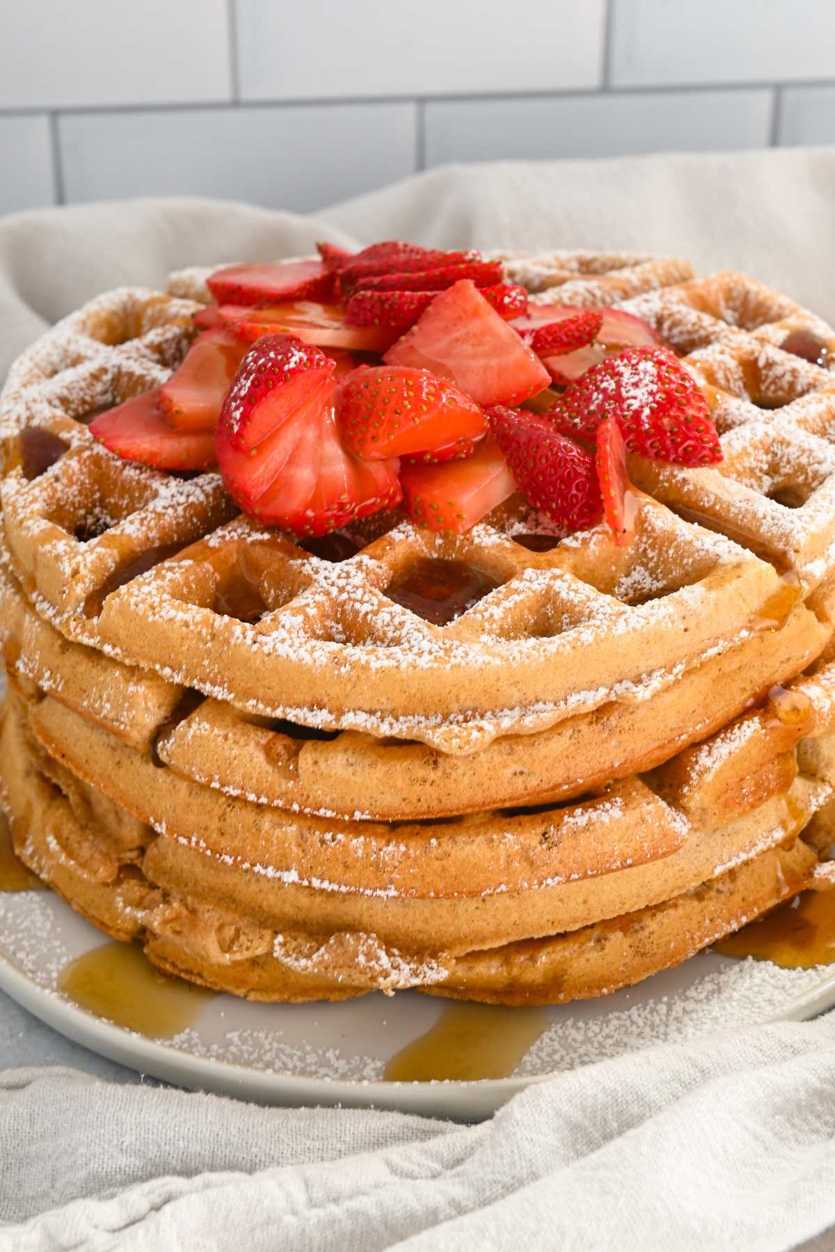 stack of kodiak waffles topped with powdered sugar, syrup and strawberries.