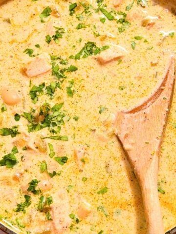 close up of white chicken chili topped with cilantro with a wooden spoon.