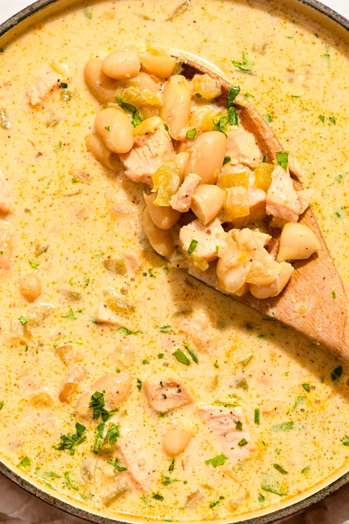 close up of white chicken chili with a wooden spoonful of it in focus.