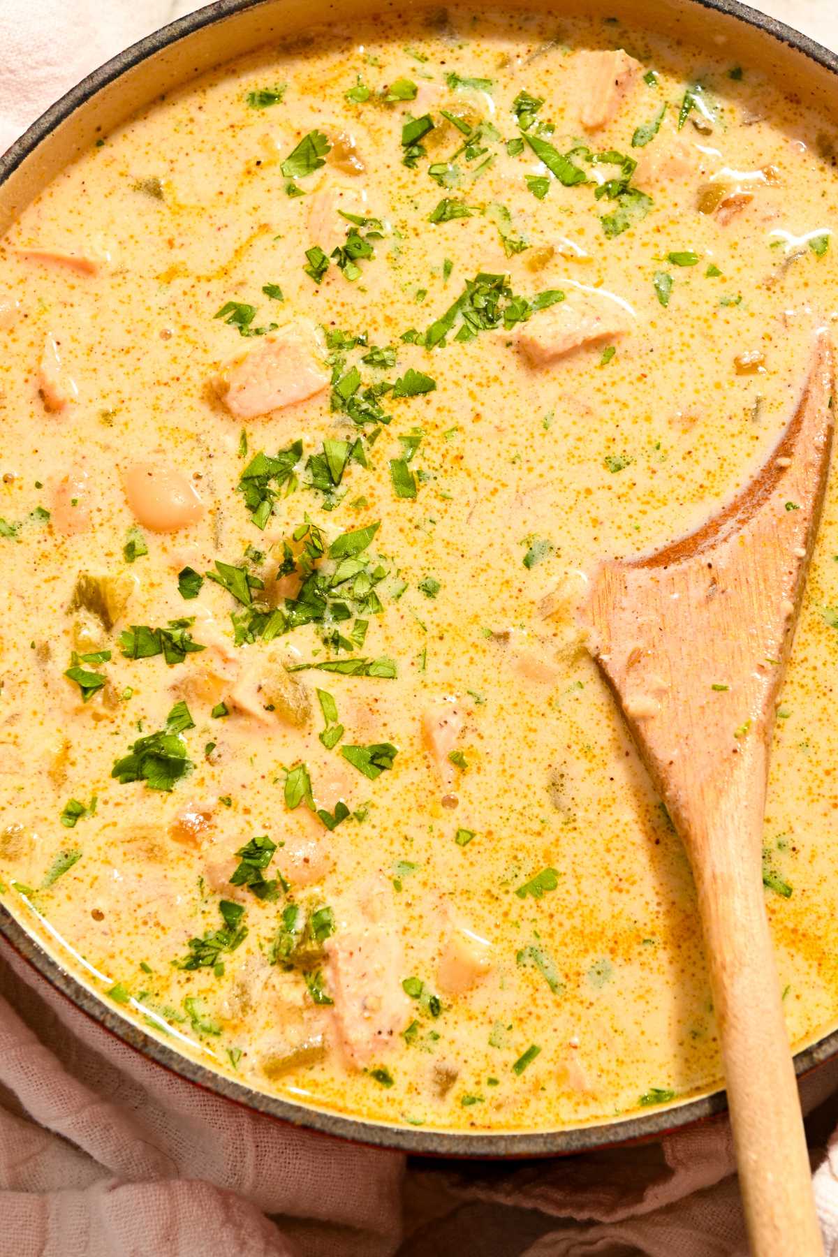 large pot of high protein white chicken chili with cilantro on top and a wooden spoon in it.