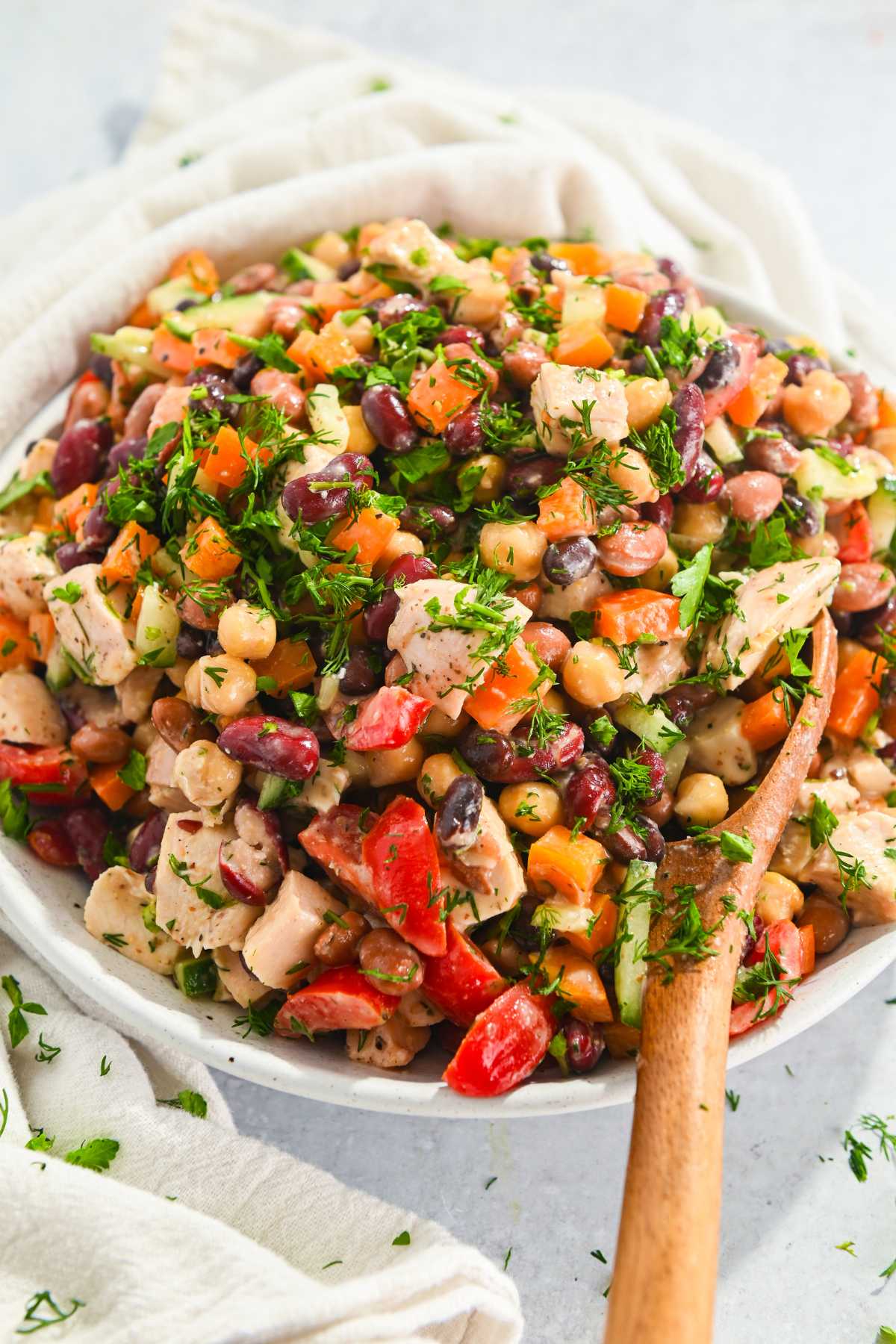 bowl of dense bean salad with chicken in a white bowl with a wooden spoon.