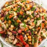 close up of a bowl of dense bean salad with chicken in a white bowl with a wooden spoon.